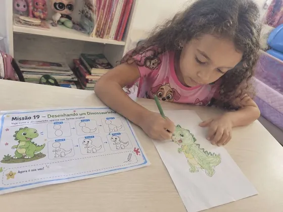 Menina desenhando um dinossauro com a lição passo a passo